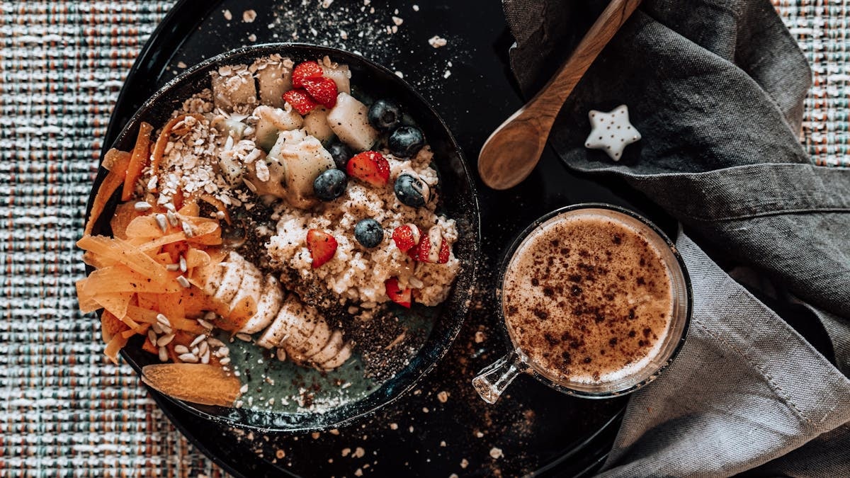 A delicious top view of a fruit and nut breakfast bowl with a fresh cup of coffee on a stylish table setting.